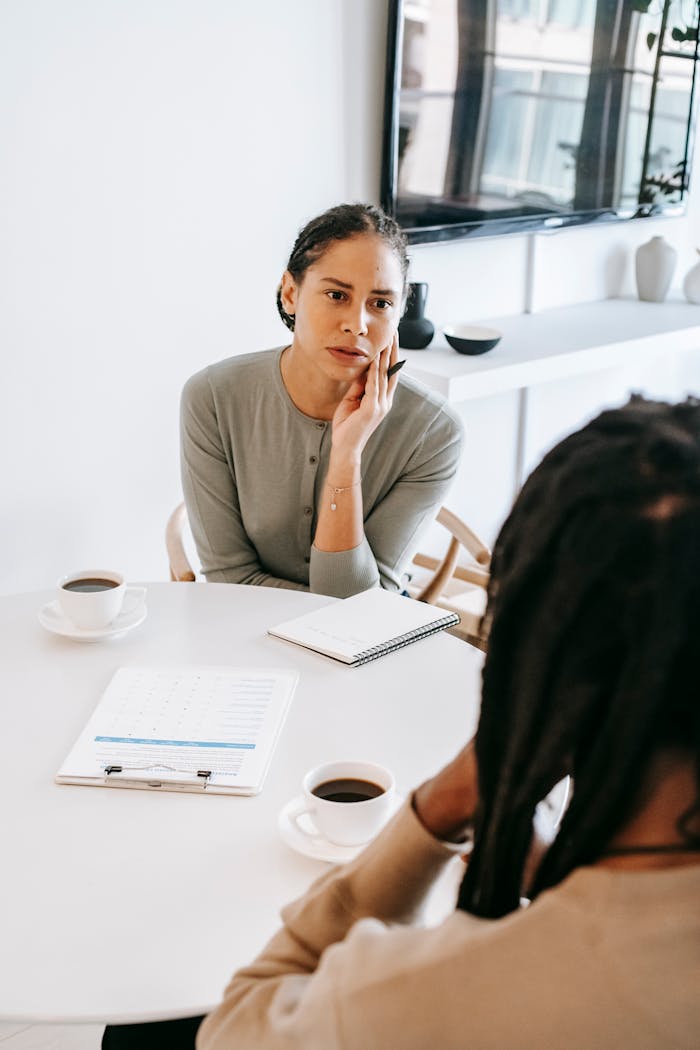 Home Serious ethnic female consultant listening to black male client problems while sitting at round table together in light psychology center