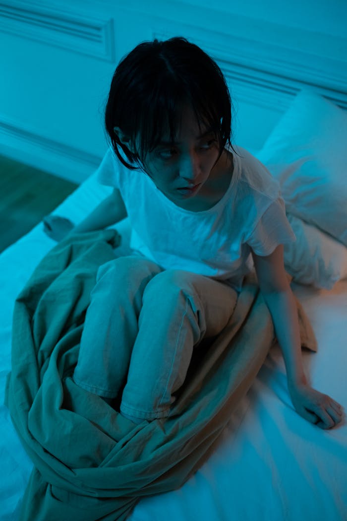 A young Asian woman sitting on bed at night feeling stressed and restless.